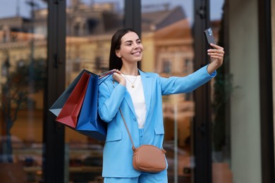 Photo of Happy woman with colorful shopping bags taking selfie outdoors