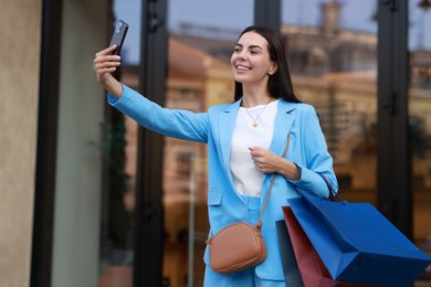 Happy woman with colorful shopping bags taking selfie outdoors