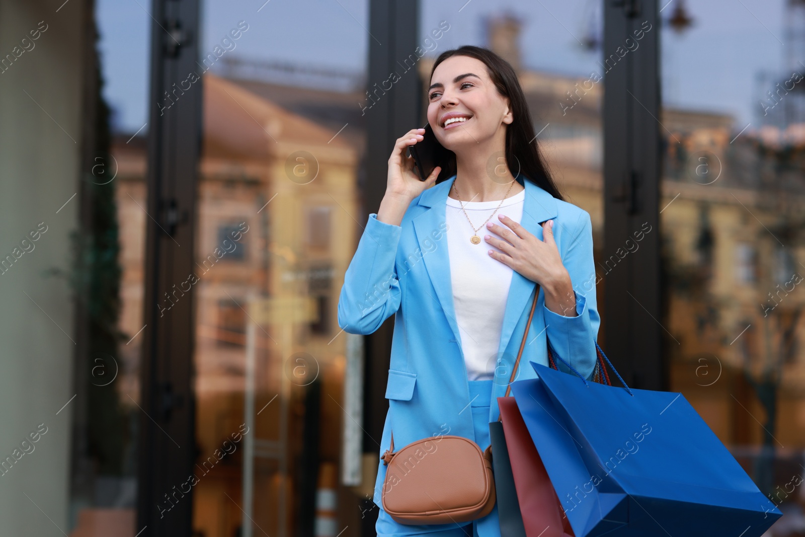 Photo of Happy woman with colorful shopping bags talking on smartphone outdoors, space for text