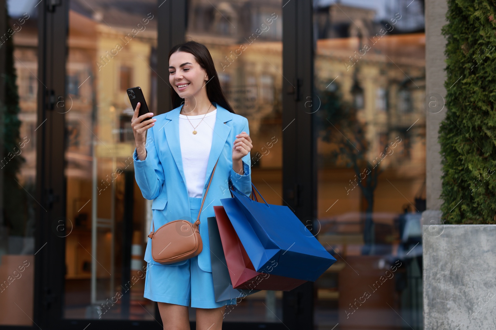 Photo of Happy woman with colorful shopping bags using smartphone outdoors