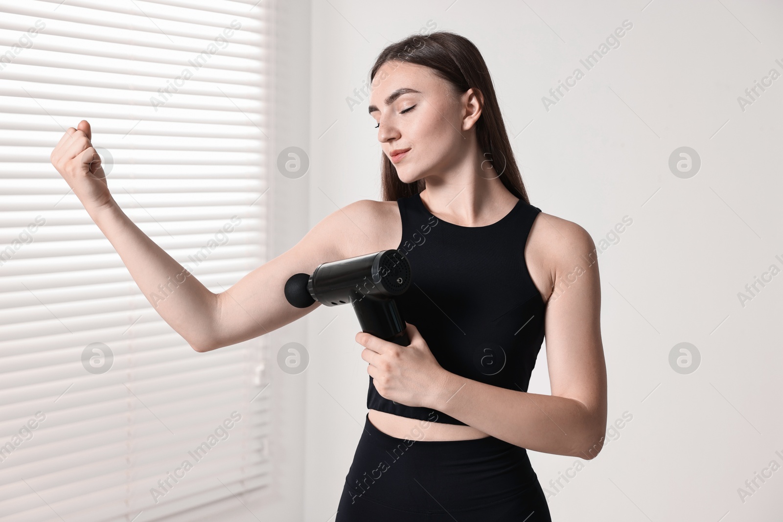 Photo of Woman using percussive massager to relax bicep indoors