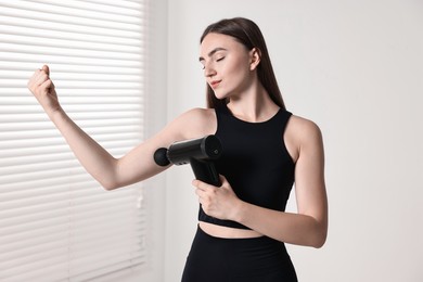 Woman using percussive massager to relax bicep indoors