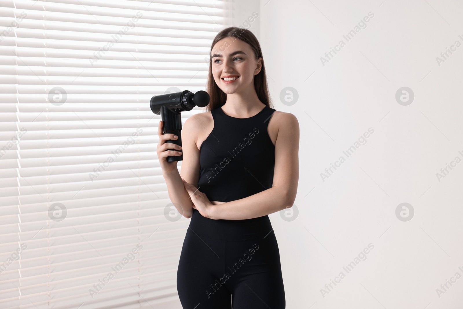 Photo of Young woman with percussive massage gun indoors