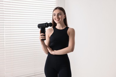 Young woman with percussive massage gun indoors