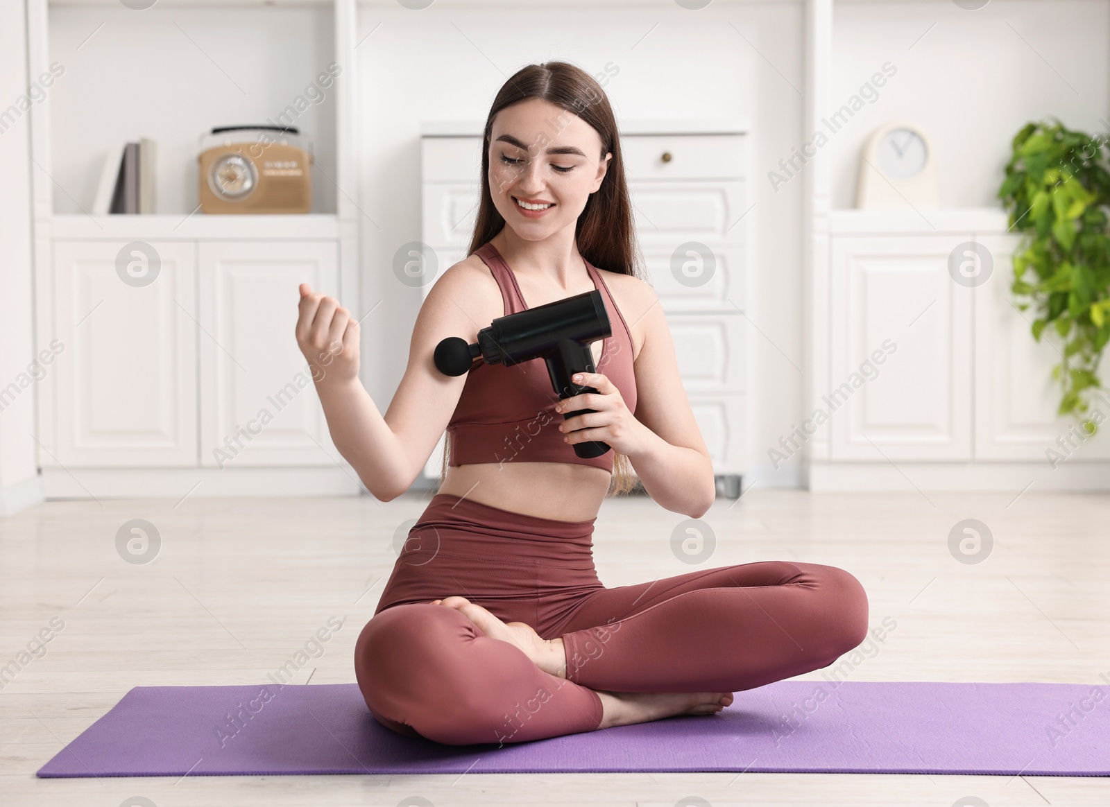 Photo of Woman using percussive massager to relieve bicep on mat at home