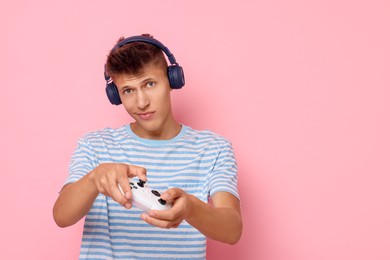 Young man in headphones playing video games with controller on pink background