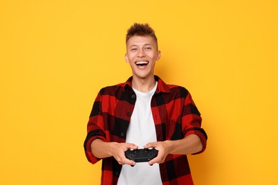 Happy young man playing video games with controller on orange background