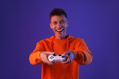 Happy young man playing video games with controller on violet background