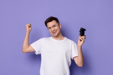 Happy young man with controller on violet background