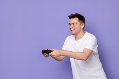 Happy young man playing video games with controller on violet background, space for text