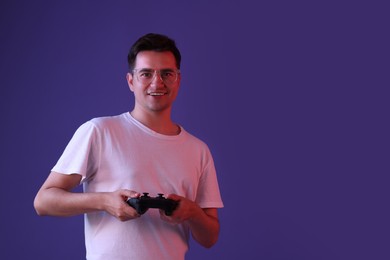 Happy young man playing video games with controller on violet background, space for text