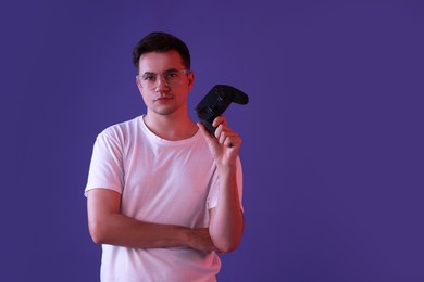 Young man with controller on violet background, space for text