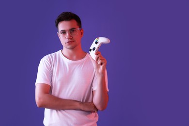 Young man with controller on violet background, space for text