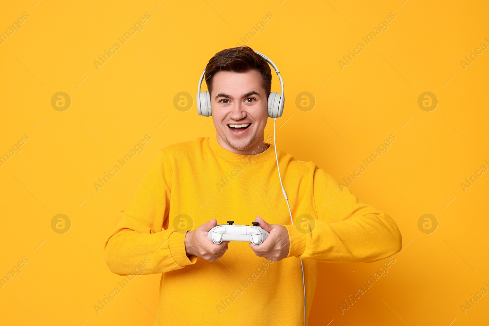 Photo of Happy young man playing video games with controller on orange background