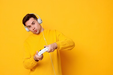 Young man in headphones playing video games with controller on orange background, space for text