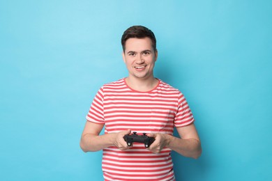 Happy young man playing video games with controller on light blue background