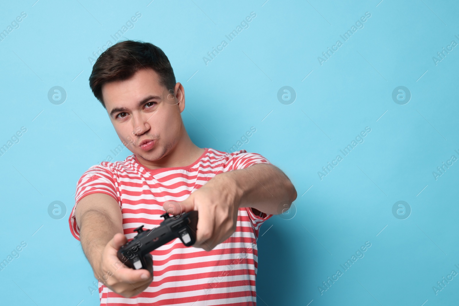 Photo of Young man playing video games with controller on light blue background, space for text