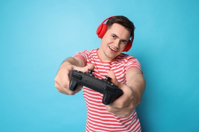 Happy young man in headphones playing video games with controller on light blue background