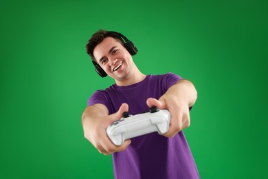 Photo of Happy young man in headphones playing video games with controller on green background