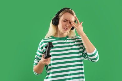 Unhappy woman in headphones with controller on green background