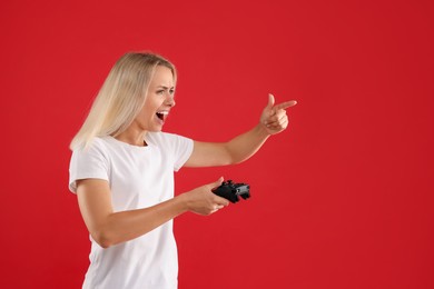 Emotional woman playing video games with controller on red background, space for text