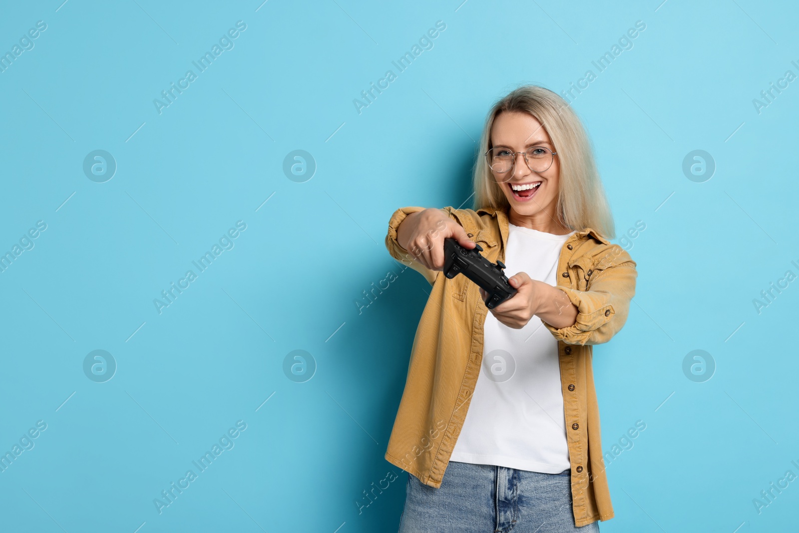 Photo of Happy woman playing video games with controller on light blue background, space for text