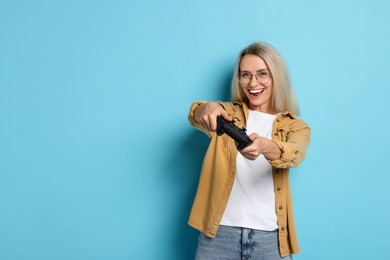 Happy woman playing video games with controller on light blue background, space for text