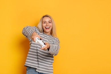 Happy woman playing video games with controller on orange background, space for text