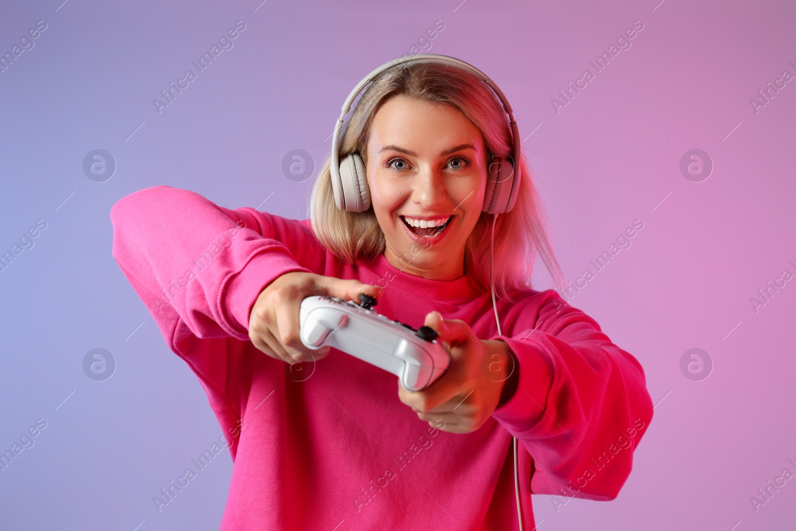 Photo of Happy woman in headphones playing video games with controller on color background