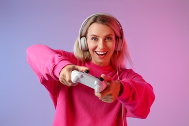 Happy woman in headphones playing video games with controller on color background