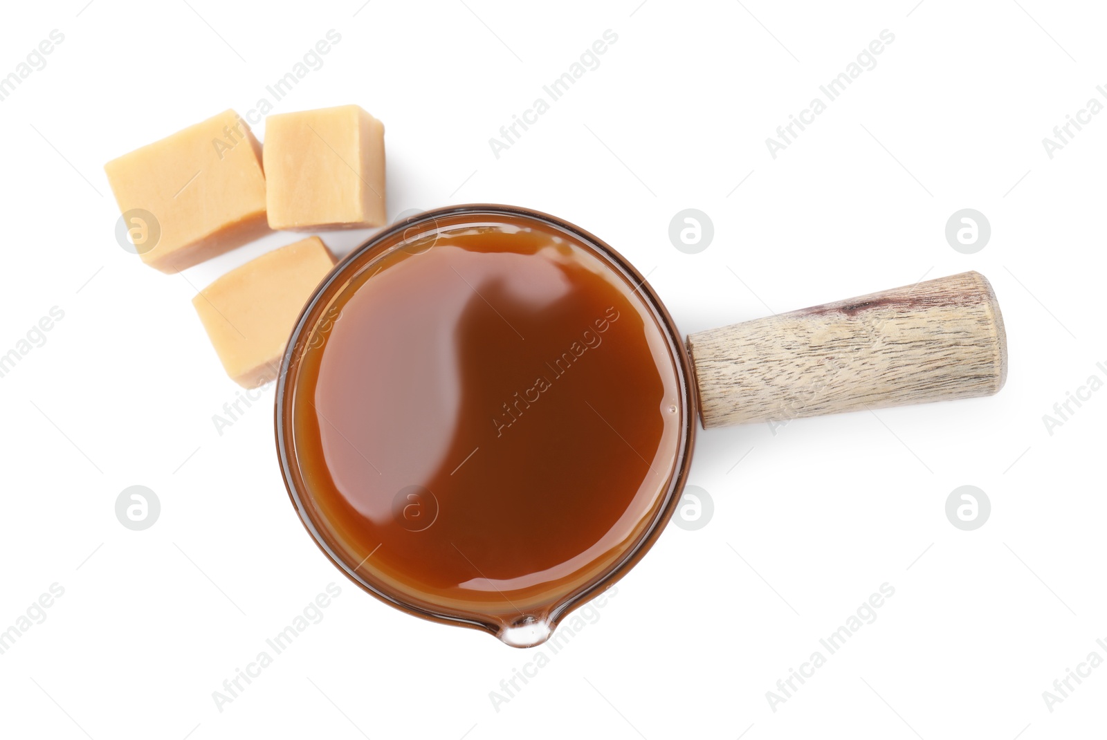 Photo of Tasty caramel sauce in glass measuring cup and sweet candies isolated on white, top view