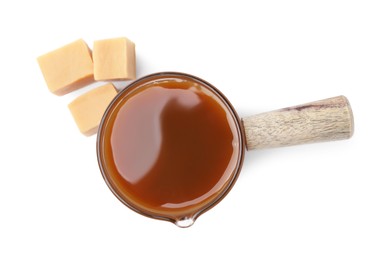 Photo of Tasty caramel sauce in glass measuring cup and sweet candies isolated on white, top view