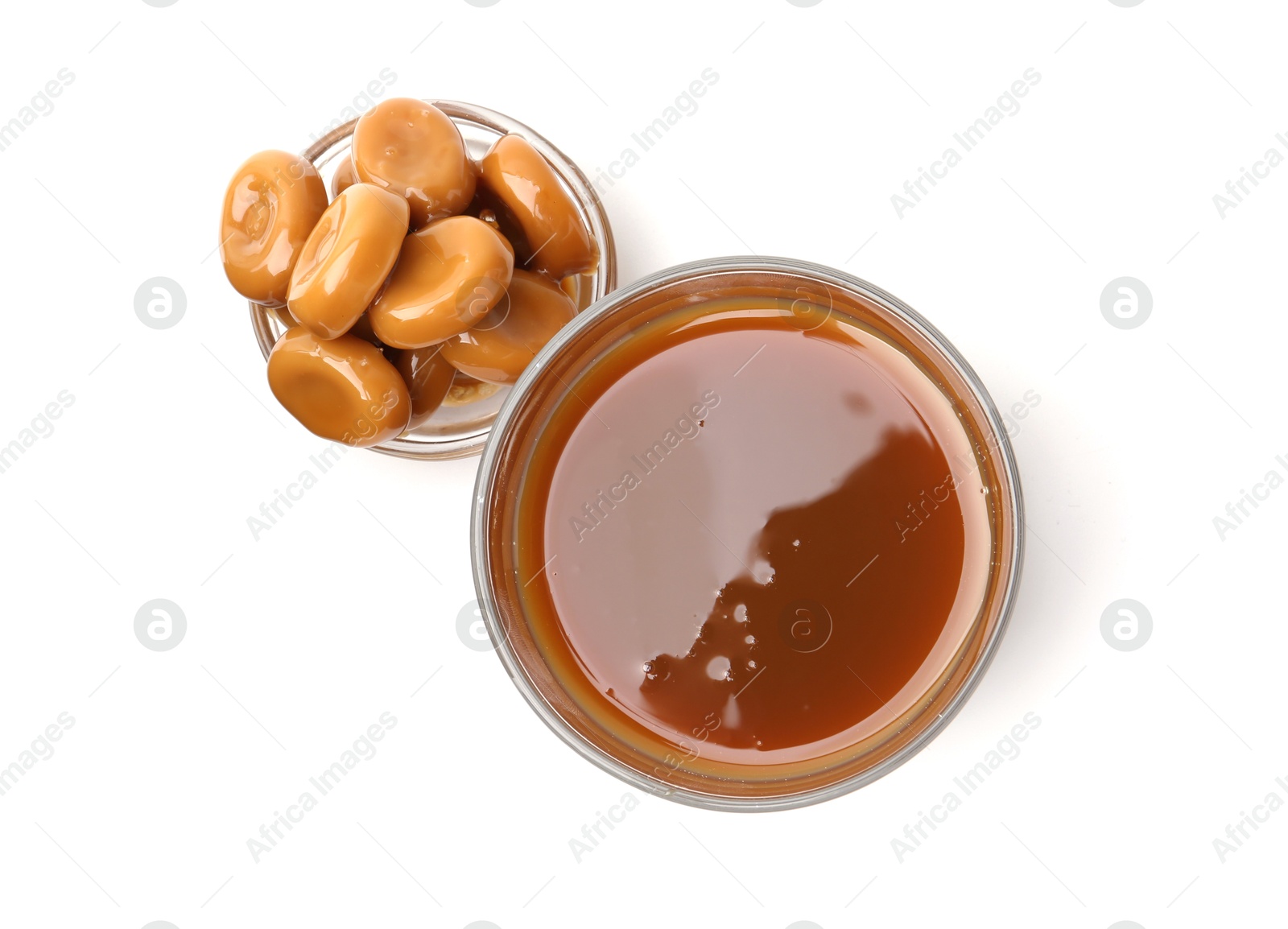 Photo of Tasty caramel sauce in glass bowl and candies isolated on white, top view