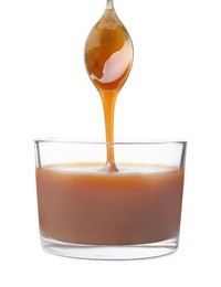 Photo of Tasty caramel sauce dripping from spoon into glass bowl on white background, closeup