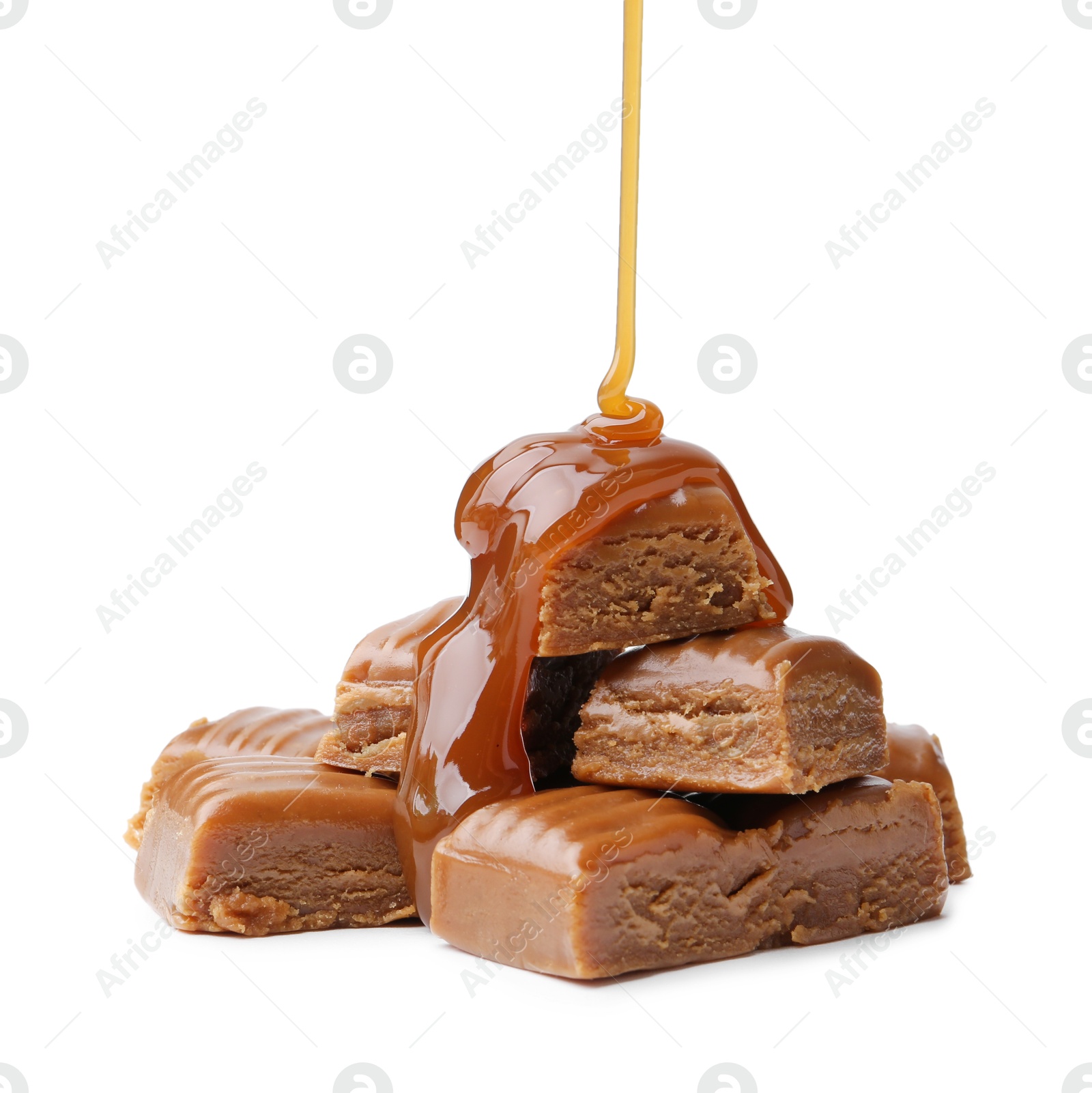 Photo of Caramel sauce dripping onto candies on white background, closeup