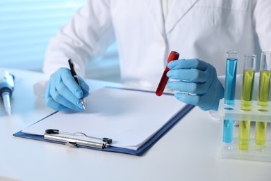 Laboratory testing. Doctor with blood sample taking notes at table indoors, closeup