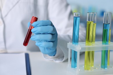 Laboratory testing. Doctor holding test tube with blood sample at table indoors, closeup