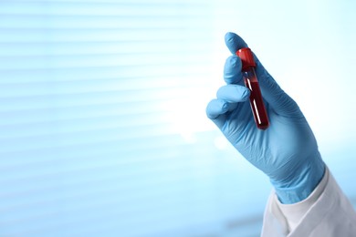 Laboratory testing. Doctor holding test tube with blood sample indoors, closeup. Space for text