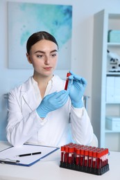 Laboratory testing. Doctor holding test tube with blood sample at table indoors