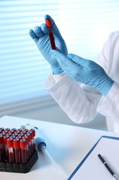 Laboratory testing. Doctor holding test tube with blood sample at table indoors, closeup