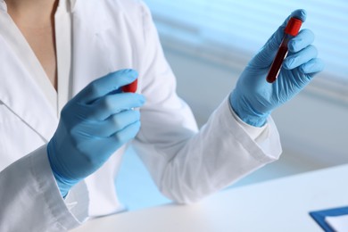 Photo of Laboratory testing. Doctor holding test tubes with blood samples at table indoors, closeup