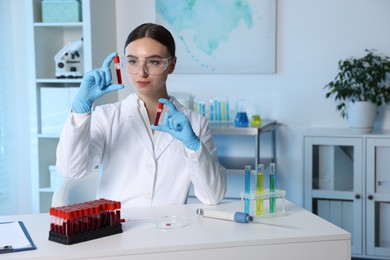 Laboratory testing. Doctor holding test tubes with blood samples at table indoors