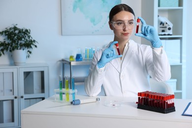 Photo of Laboratory testing. Doctor holding test tubes with blood samples at table indoors