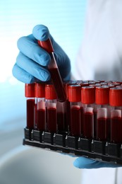 Photo of Laboratory testing. Doctor taking test tube with blood sample from rack indoors, closeup