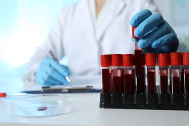 Laboratory testing. Doctor taking test tube with blood sample while working at table indoors, closeup