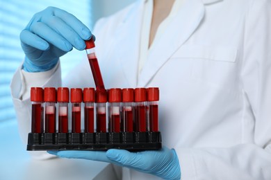 Photo of Laboratory testing. Doctor taking test tube with blood sample from rack indoors, closeup