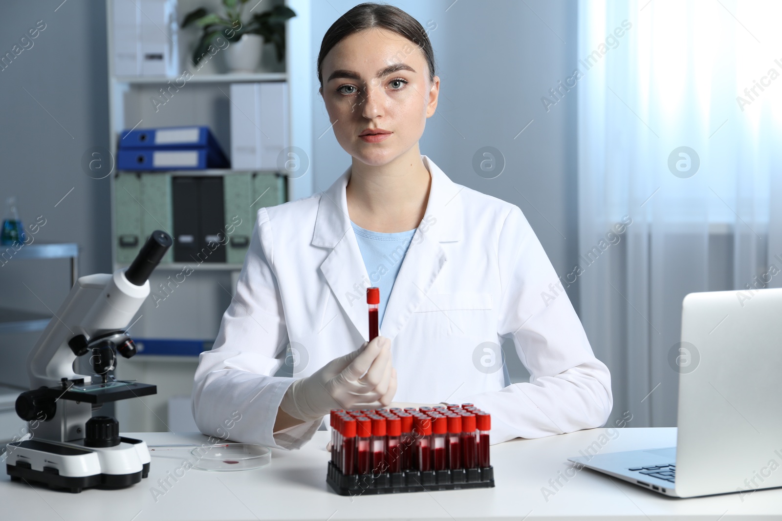 Photo of Laboratory testing. Doctor holding test tube with blood sample at table indoors