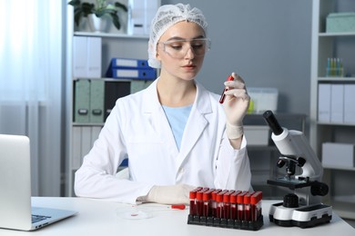 Laboratory testing. Doctor holding test tube with blood sample at table indoors