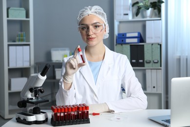 Photo of Laboratory testing. Doctor holding test tube with blood sample at table indoors