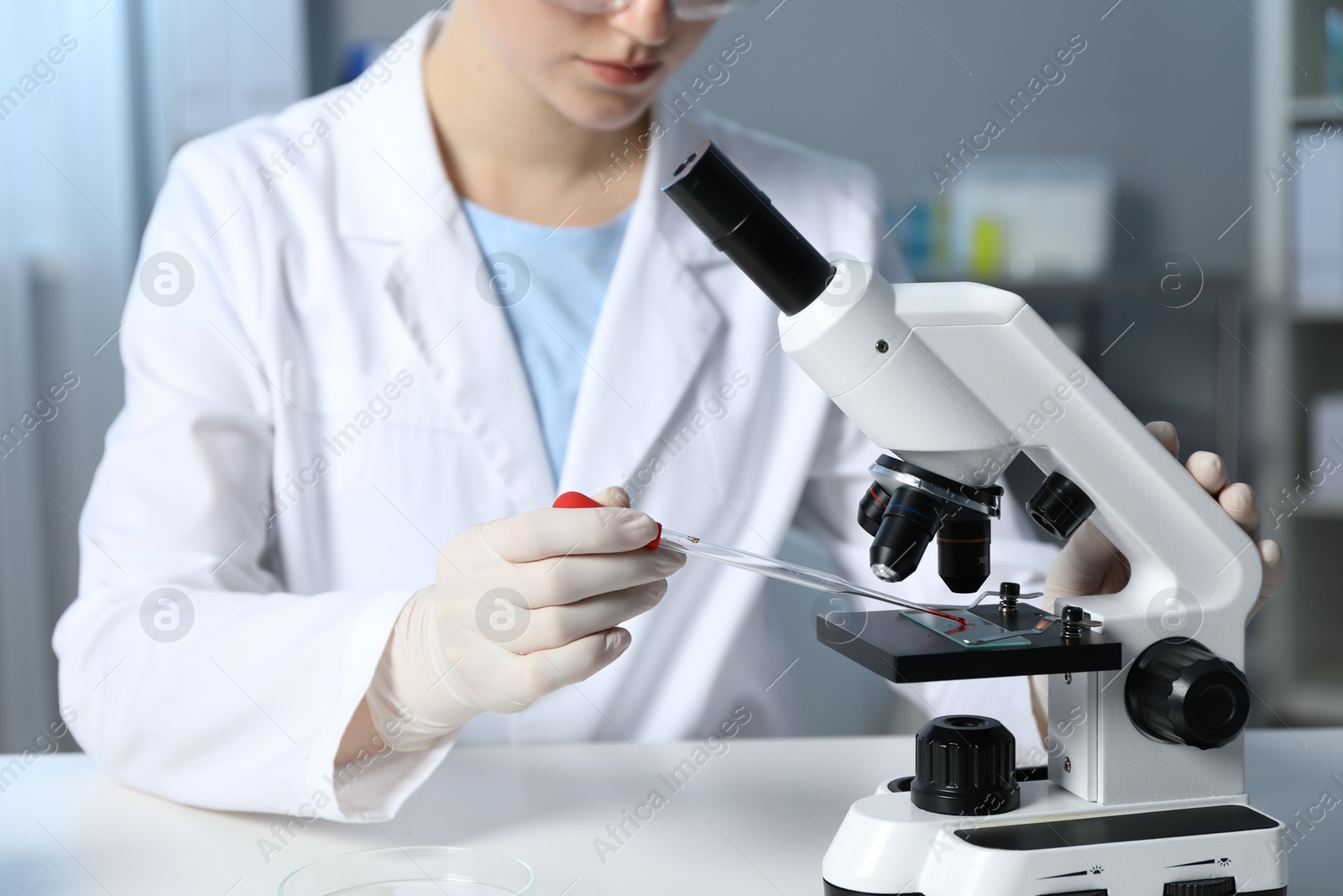 Photo of Laboratory testing. Doctor dripping blood sample onto glass slide while working with microscope at table indoors, closeup